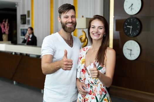 Young couple, husband and wife, check into a hotel and give a thumbs up.