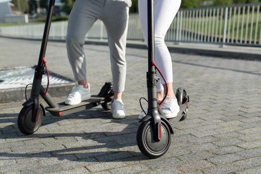 A couple of men and women are walking in the Park and standing near electric scooters.