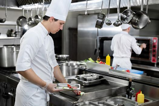 Professional chef in the kitchen roasts vegetables on the grill