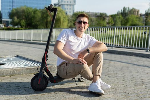 Cheerful man is sitting on an electric scooter in a park