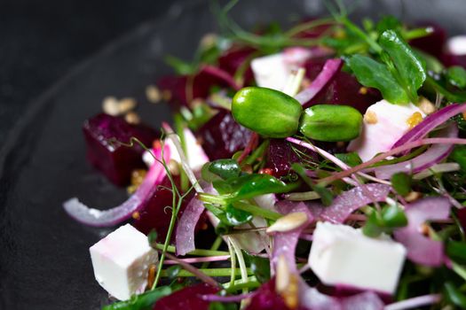 Salad of microgreen, beetroot and cheese with fresh onions and seeds on a plate.