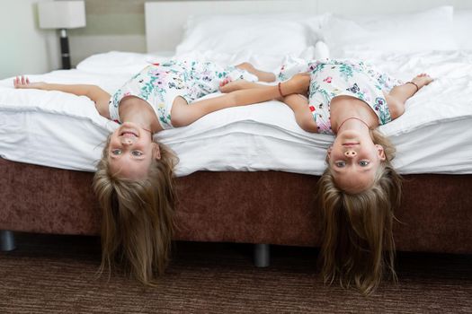 Two twin sisters are lying on the bed upside down.