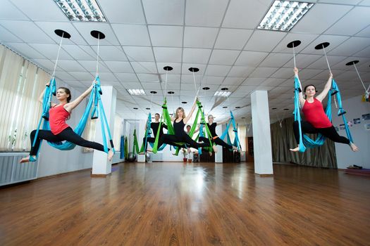 Group of young people practicing yoga on hammock at health club. Fitness, stretch, balance