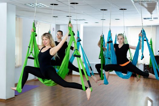 Group of young people practicing yoga on hammock at health club. Fitness, stretch, balance