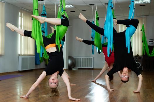 Group of young beautiful yogi women doing aerial yoga practice in hammocks in fitness club.