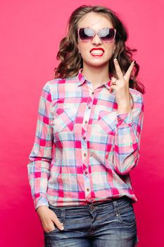 Portrait of emotional girl posing at camera, showing tooth and peace by fingers. Beautiful, swag woman with curly hair,red lips wearing in cheked. Shopping and fashion.