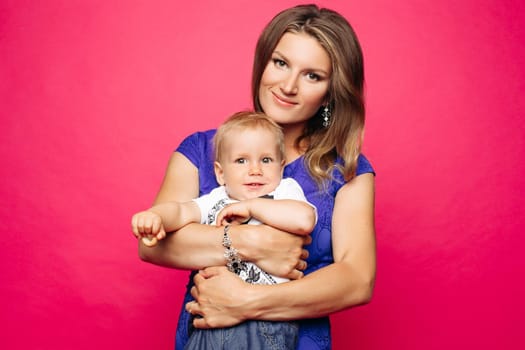 Beautiful young mom with little child, holding anf posing, looking at camera. Pretty and stylish mother loving, embracing her little son. Concept of parent s day, family look and relationship.