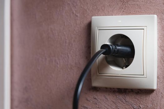 Close-up of a black electric plug in a 220 socket in the wall. Power on concept.