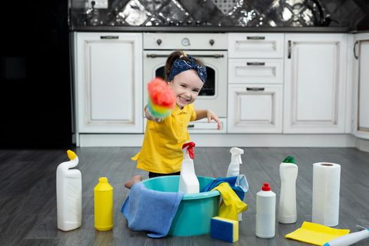 A little housewife with a dusty brush and detergents in the kitchen.