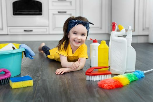 A little girl is playing with cleaning products at home in the kitchen.