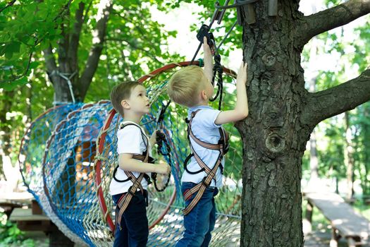A little boy helps his friend with equipment in a rope park.