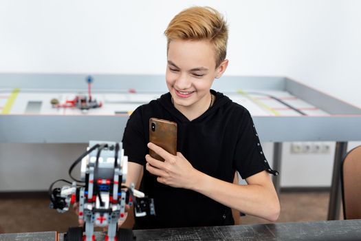 Student builds a robot constructor from plastic parts programmed on a computer during a robotics lesson at school and takes pictures on the phone