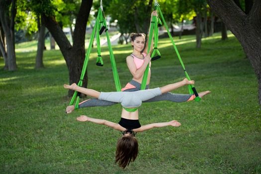 Happy cute young woman doing aerial yoga with her little sister in the park