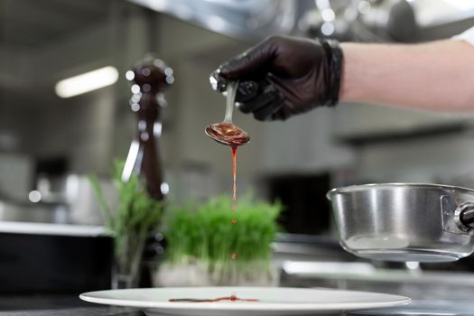 Chef pours red strawberry sauce into a plate