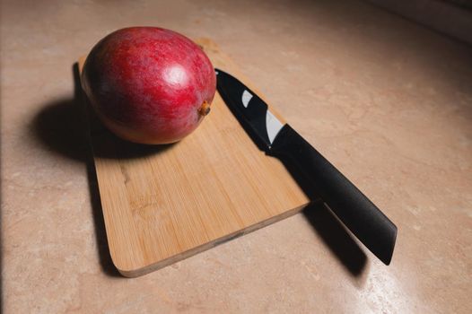 A ripe whole mango fruit lies on a cutting board next to a kitchen knife. Preparing a healthy snack. natural food antioxidants.