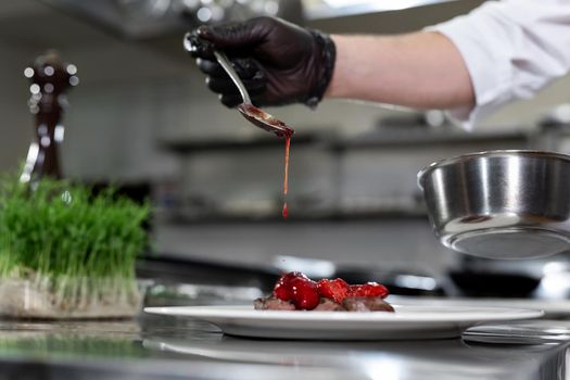 Hand holds spoon over meat. Sauce of red color. Delicious medallions with strawberries