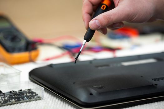 Close-up of a male engineer repairing a laptop in the workshop, disassembling the laptop cover with a screwdriver