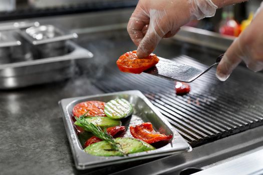 Professional chef in the kitchen roasts vegetables on the grill