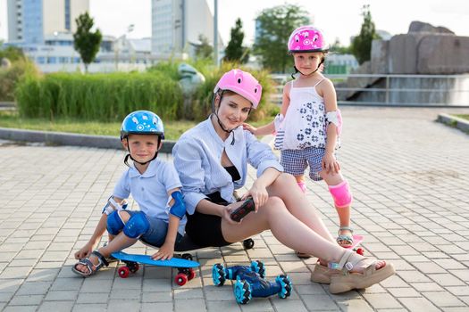A mother with children in helmets sit on a skateboard and play in the Park with a robot car that is controlled by a glove.