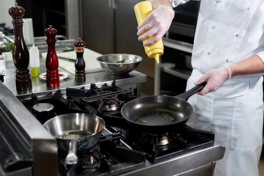 Chef pours olive oil from a bottle into a frying pan