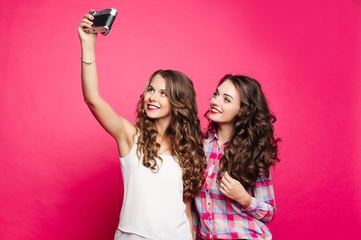 Studio Portrait of happy nice girls in retro style with long wavy hair. Giving selfie to an old film camera. The brunette in a checkered shirt makes an emphasis on the hair holding them by hand.