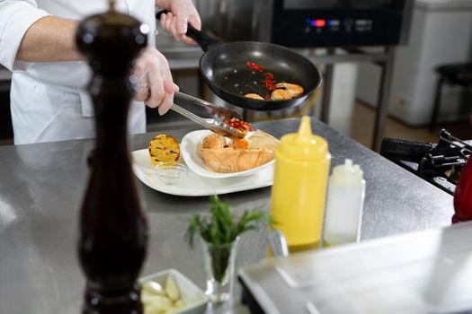 Beautiful man chef preparing dish with shrimps at table in kitchen