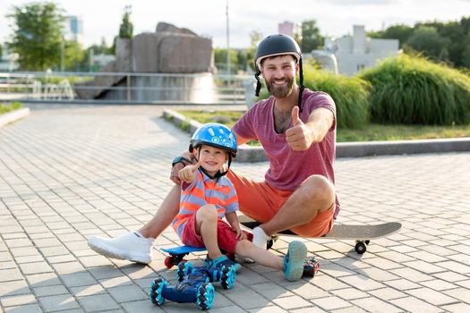 Happy father and son in helmets play in the Park with a robot car that is controlled by a glove while sitting on skateboards.