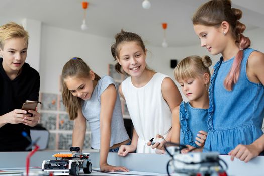 Portrait of happy children at school in the office at a robotics lesson, with a modern office with computers in the background