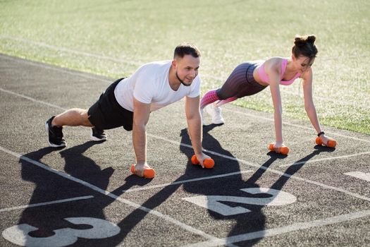 Man and a woman train with dumbbells at the stadium in the summer. Sports lifestyle