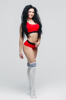 Attractive long curly haired girl in sports red wear and white leggins. Sexy and hot woman with perfect body sedactive posing against whitae background. Concept of sport, dance, helthy lifestyle.