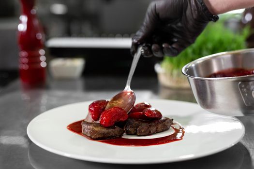 Chef decorates meat with strawberries in a professional kitchen.