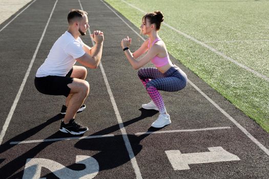 Young sports couple trains at the stadium in the summer at sunset, warm up and squat. Sport. Fitness