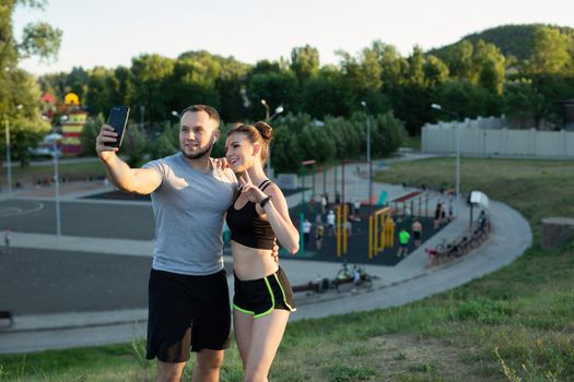 Young happy man and woman take a selfie on the phone in the park on the background of the sports field