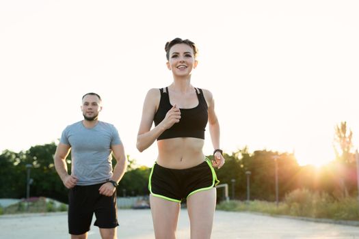 Woman and a man run in the park at sunset