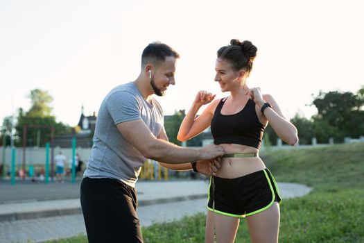 Man measures a young woman's waist with a measuring tape at a stadium at sunset