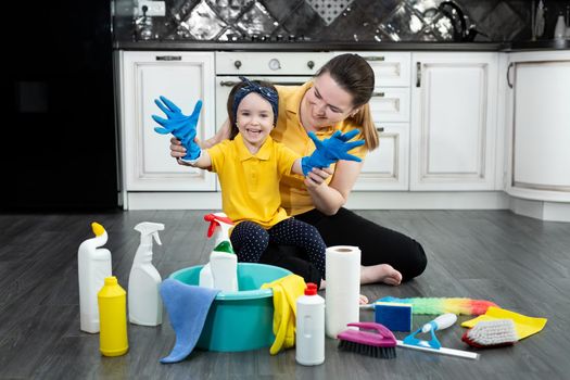 Happy mother and her daughter put on rubber gloves and enjoy cleaning, having fun together