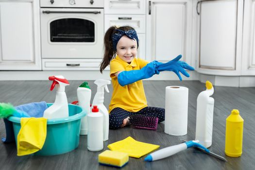 A little girl puts on gloves while cleaning the kitchen.