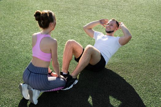 Man and a woman pump their abs in the park on the grass