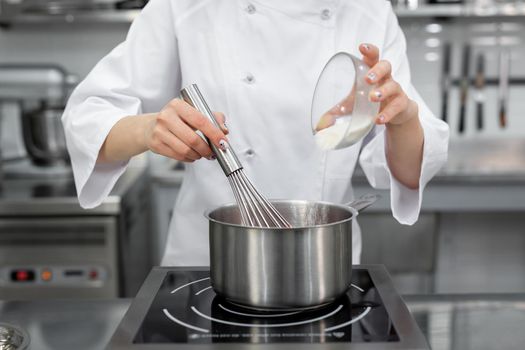 Pastry chef adds sugar to the saucepan with strawberry puree.