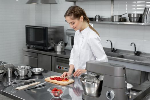 A pastry chef in a professional kitchen cuts strawberries for dessert