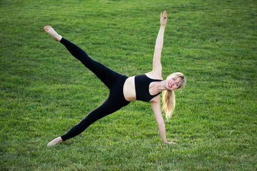 Attractive young caucasian woman standing in yoga pose on the grass