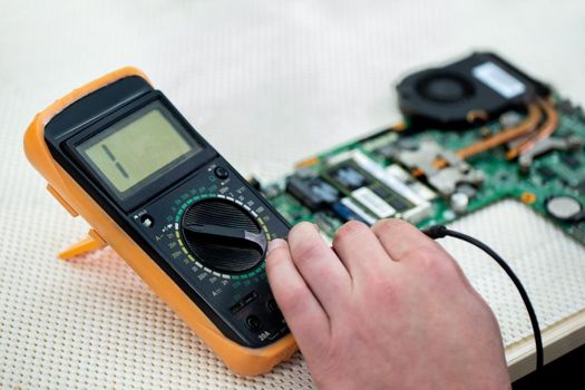 The master checks a broken laptop with a multimeter