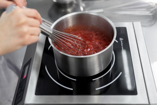 Pastry chef cooks strawberry puree with sugar in a saucepan.