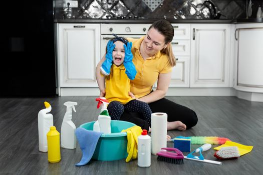 Happy mother and her daughter put on rubber gloves and enjoy cleaning, having fun together