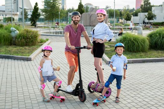 Happy family with kids riding on Segways, electric scooter and skateboards in the Park in the summer, children eating ice cream.