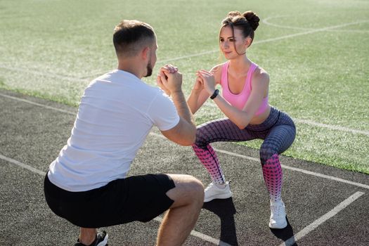 Young sports couple trains at the stadium in the summer at sunset, warm up and squat. Sport. Fitness