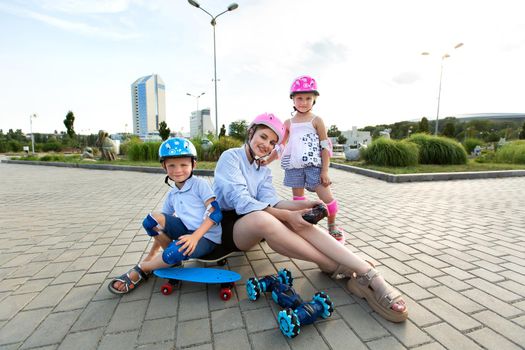 A mother with children in helmets sit on a skateboard and play in the Park with a robot car that is controlled by a glove.