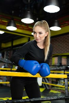 Female boxer having muscular body standing inside a boxing ring. Boxer resting her arms on the rope of boxing ring.