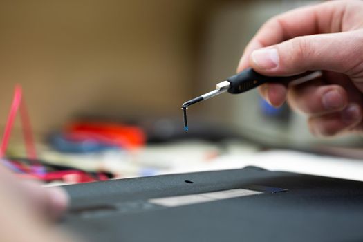 Close-up of a male engineer repairing a laptop in the workshop, disassembling the laptop cover with a screwdriver