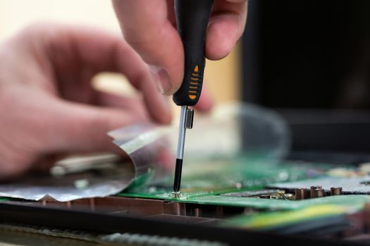 Young male tech or engineer repairs electronic equipment in research facility. A man disassembles a computer with a magnetic screwdriver